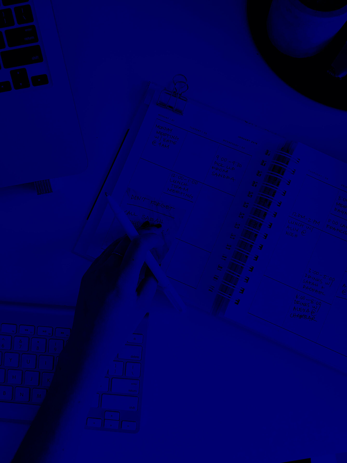 Main écrivant dans un agenda avec un clavier d'ordinateur en arrière-plan